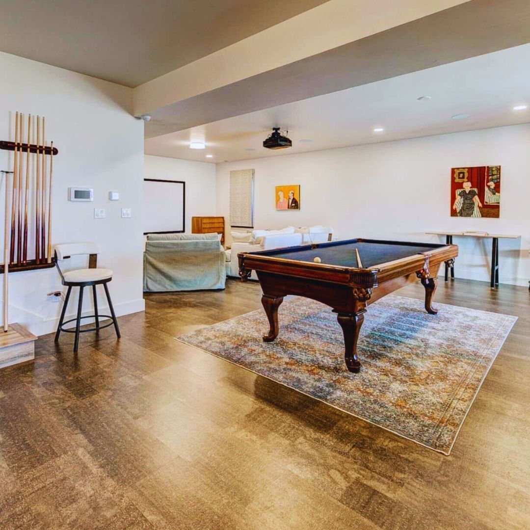 Spacious rec room with pool table, seating, artwork, and cue rack on wood flooring.