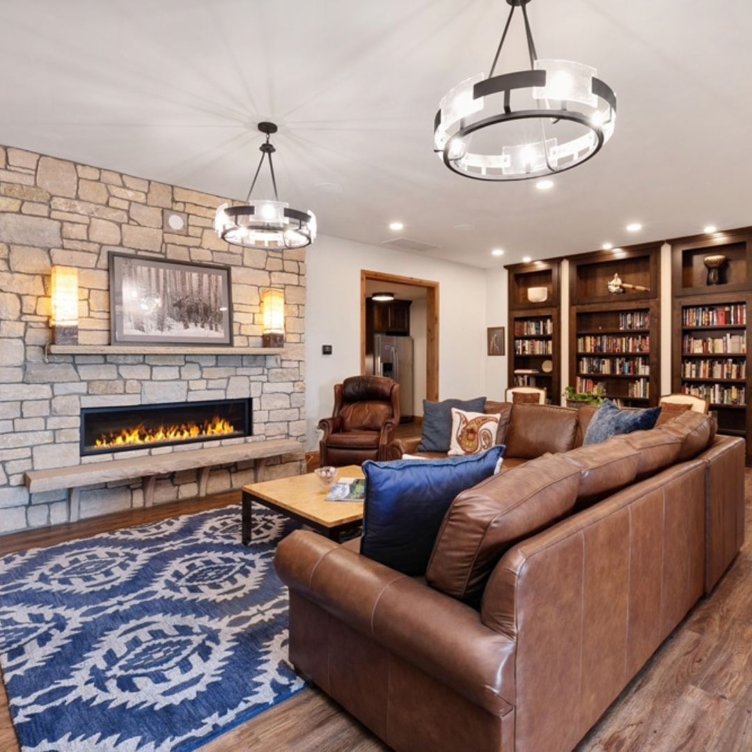 Living room with fireplace, library, leather sofa, blue rug, and circular chandeliers.