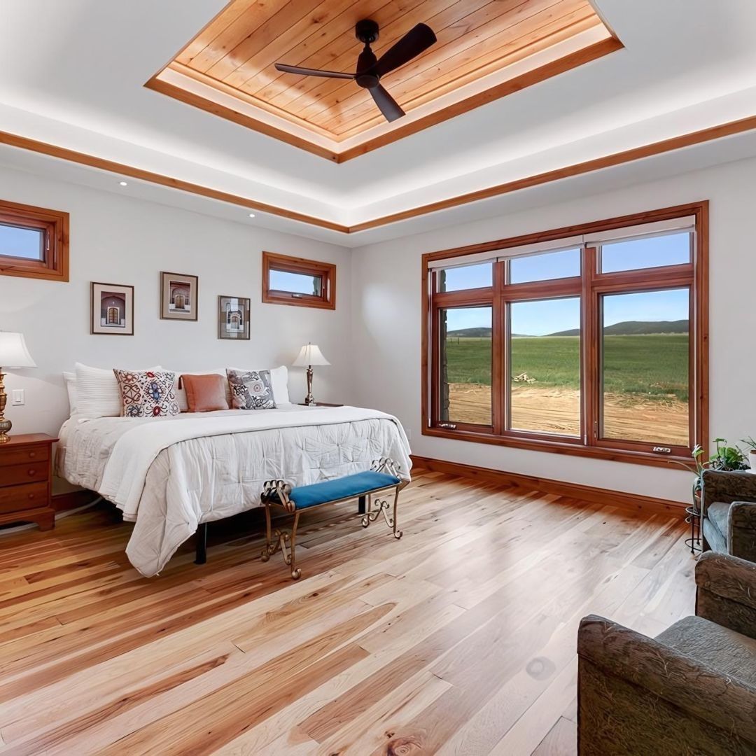Bedroom with wood ceiling, light wood floor, and large window overlooking a field.