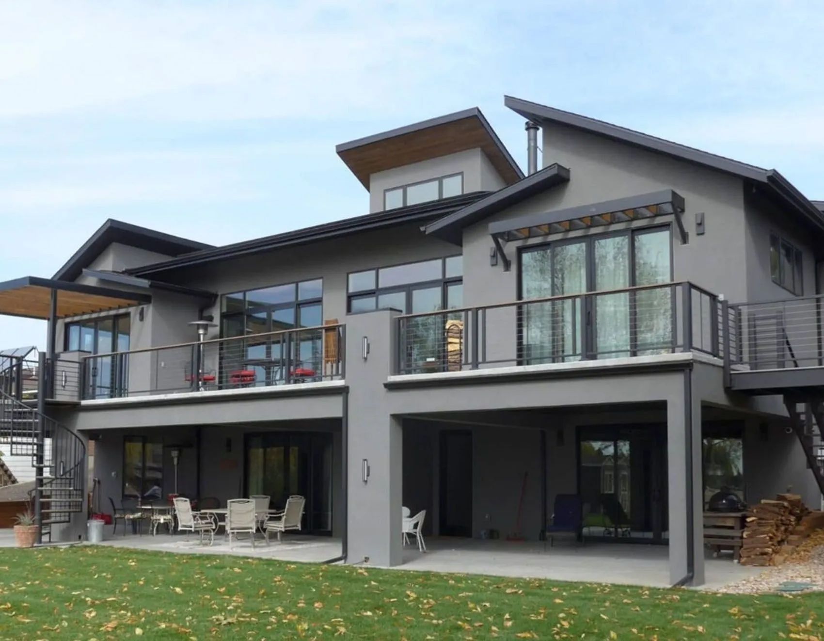 Modern gray house with balconies, multiple levels, and a sloping roof against a cloudy sky.