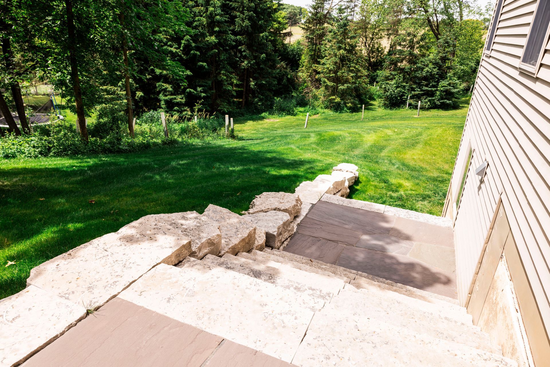 Concrete stairs leading down from a house to a grassy backyard with trees.