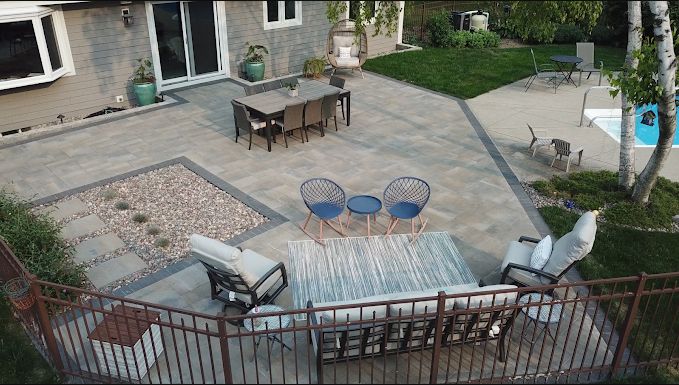 High-angle view of a backyard patio with a dining table, outdoor lounge seating, a gravel garden feature, and a pool.
