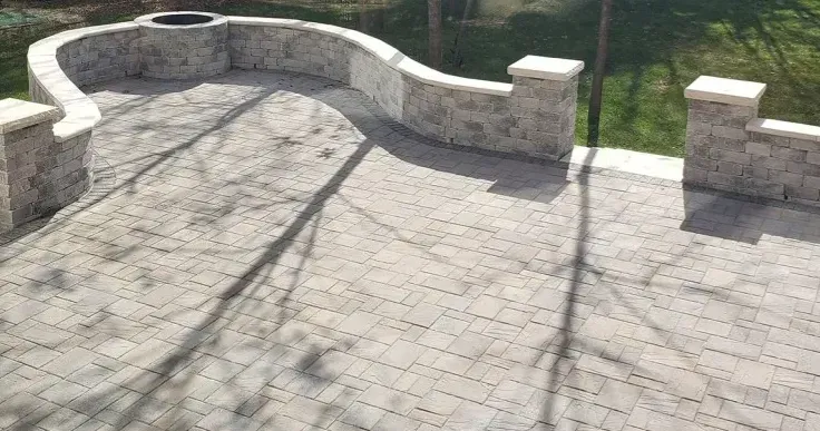 A curved stone patio with a built-in fire pit and retaining wall, featuring decorative pillars and a paved stone floor.