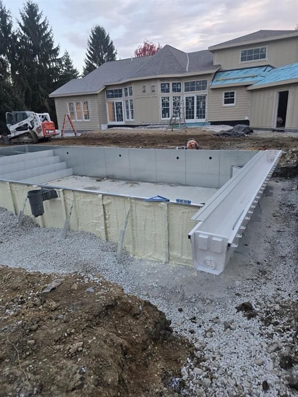 A partially built backyard swimming pool with gray panels and a beige house in the background.