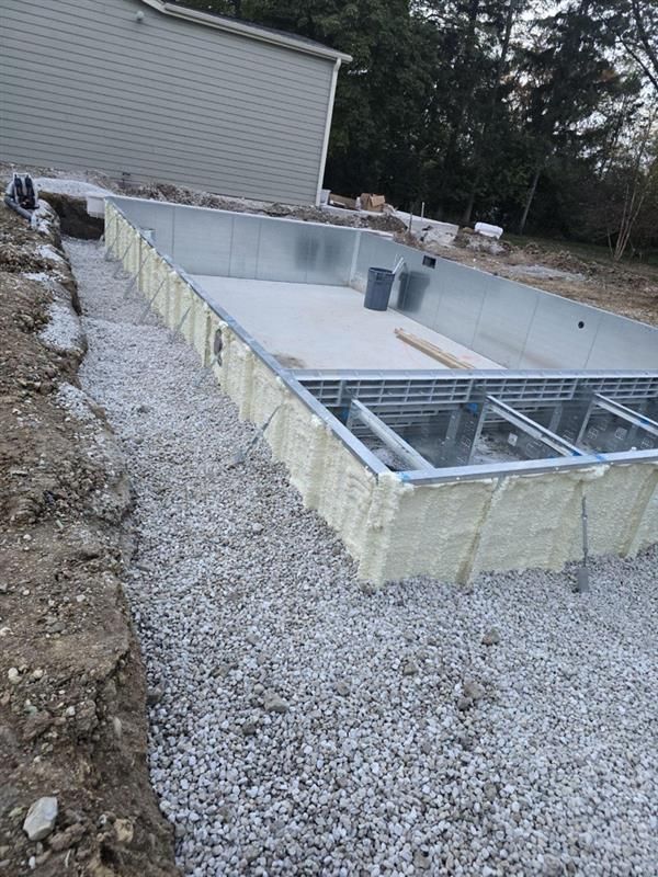 An outdoor construction site shows an in-ground swimming pool frame surrounded by gravel and foam insulation.
