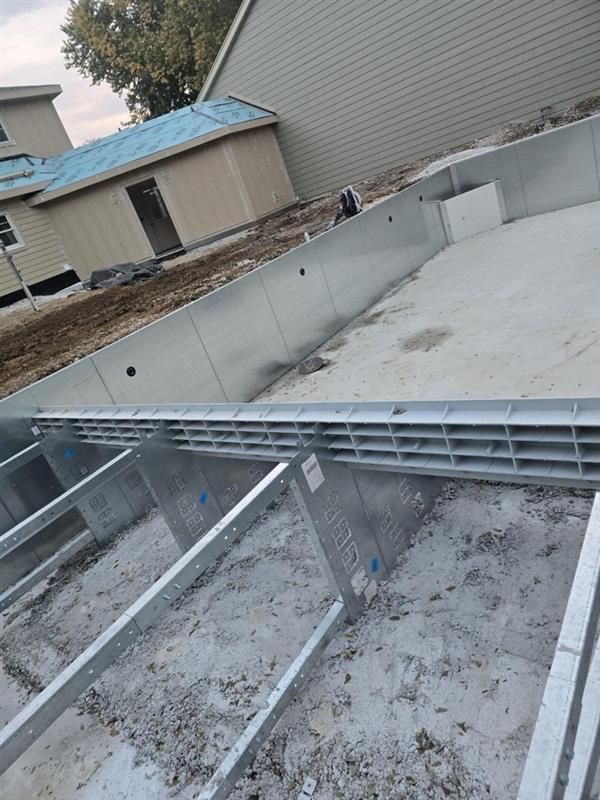 An in-ground swimming pool under construction, showing metal wall panels and structural supports on a concrete base.