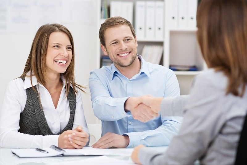 A man and woman are shaking hands with a woman while sitting at a table.