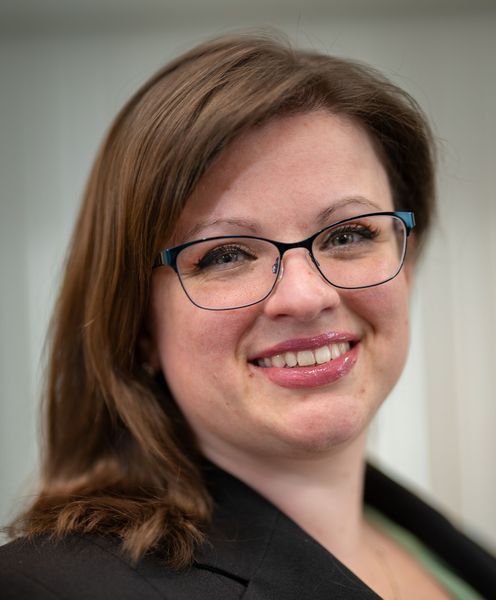 Woman with glasses smiling, wearing a black blazer.