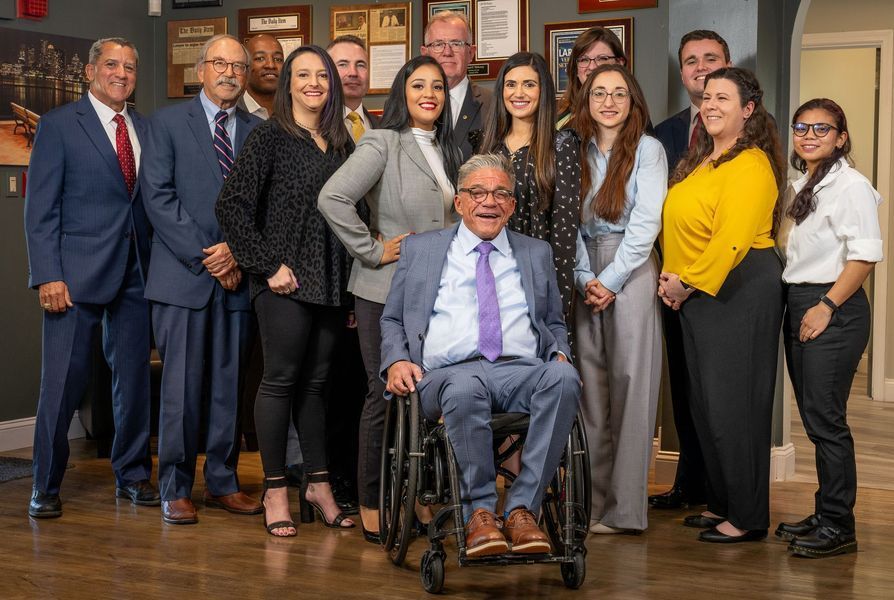A group of people, some smiling, pose for a photo in an office setting. A man in a wheelchair is in the center.