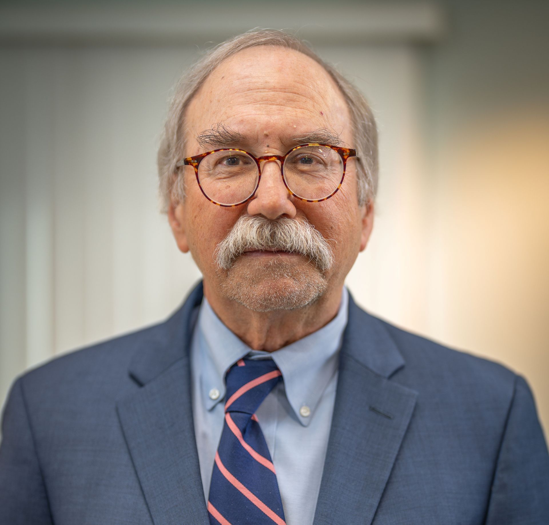 Man in blue suit, glasses, and tie, looking at the camera.