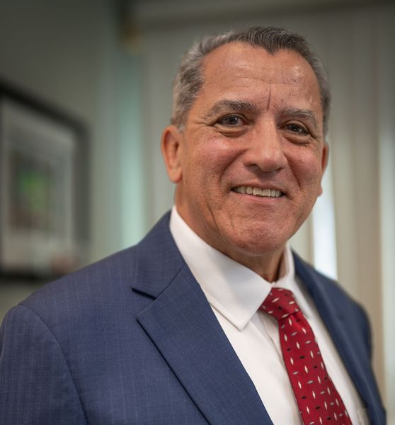Man in blue suit, red tie, smiling at camera. Indoor setting, possibly office.