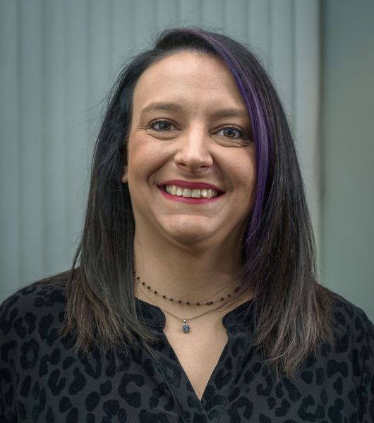 Woman with dark hair smiling, purple highlights, wearing a black shirt with animal print.