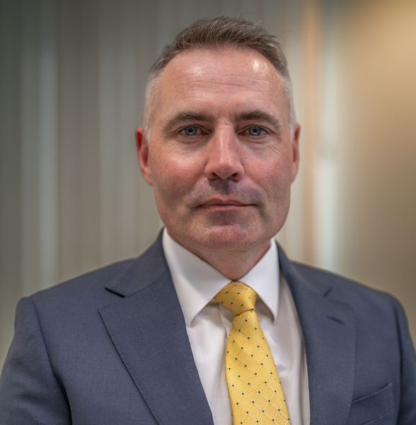 Man in a blue suit and yellow tie, looking directly at the camera.