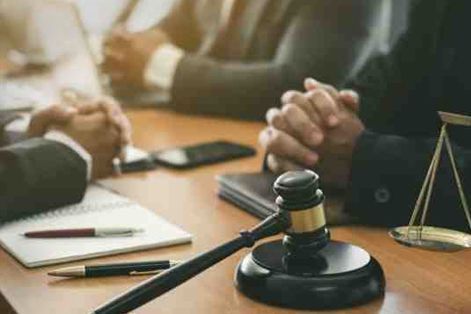 Gavel, scales, and notebook on a table with people, likely lawyers, in suits.