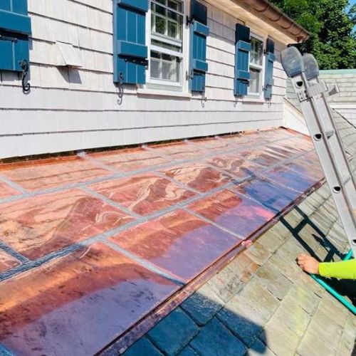 Worker sealing a roof with reflective waterproof membrane beside a white house with blue shutters