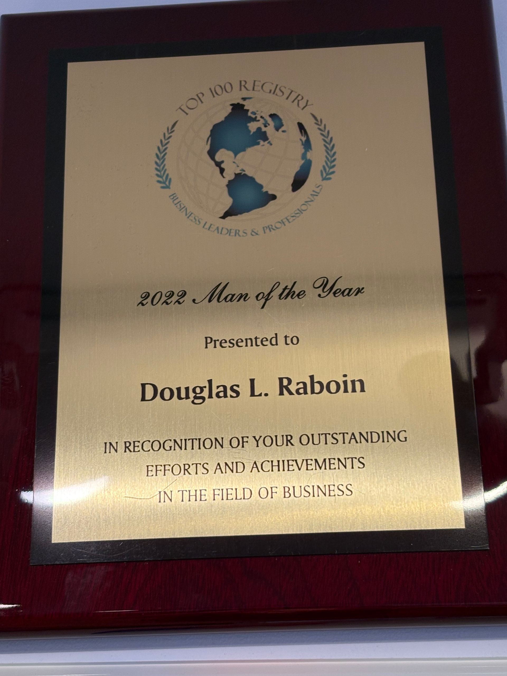 Framed gold plaque award reading “2012 Man of the Year” with globe logo and recipient name Douglas L. Raboin