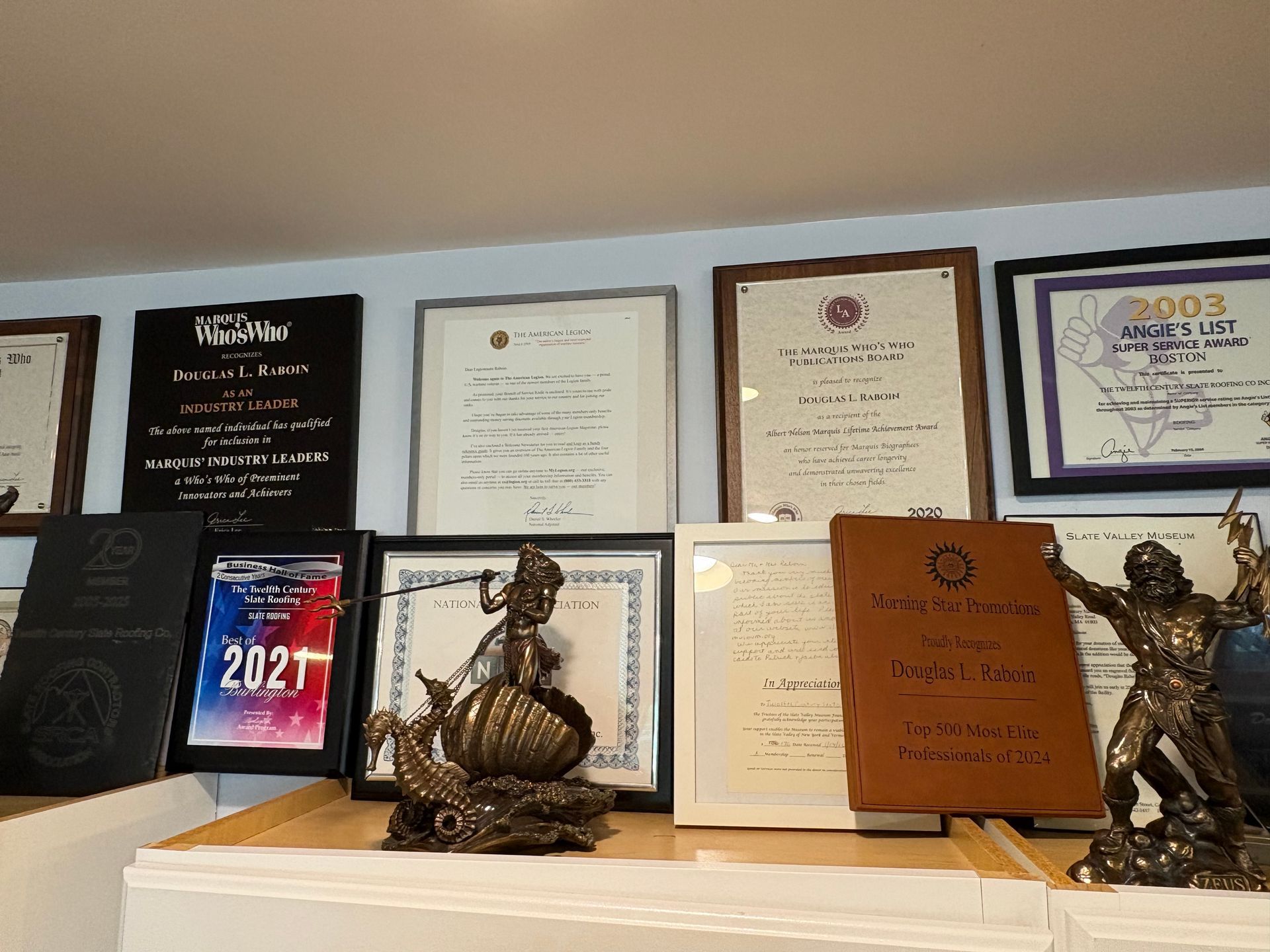 Wall of framed certificates and awards on a shelf, with decorative statues and a tablet showing “2021”