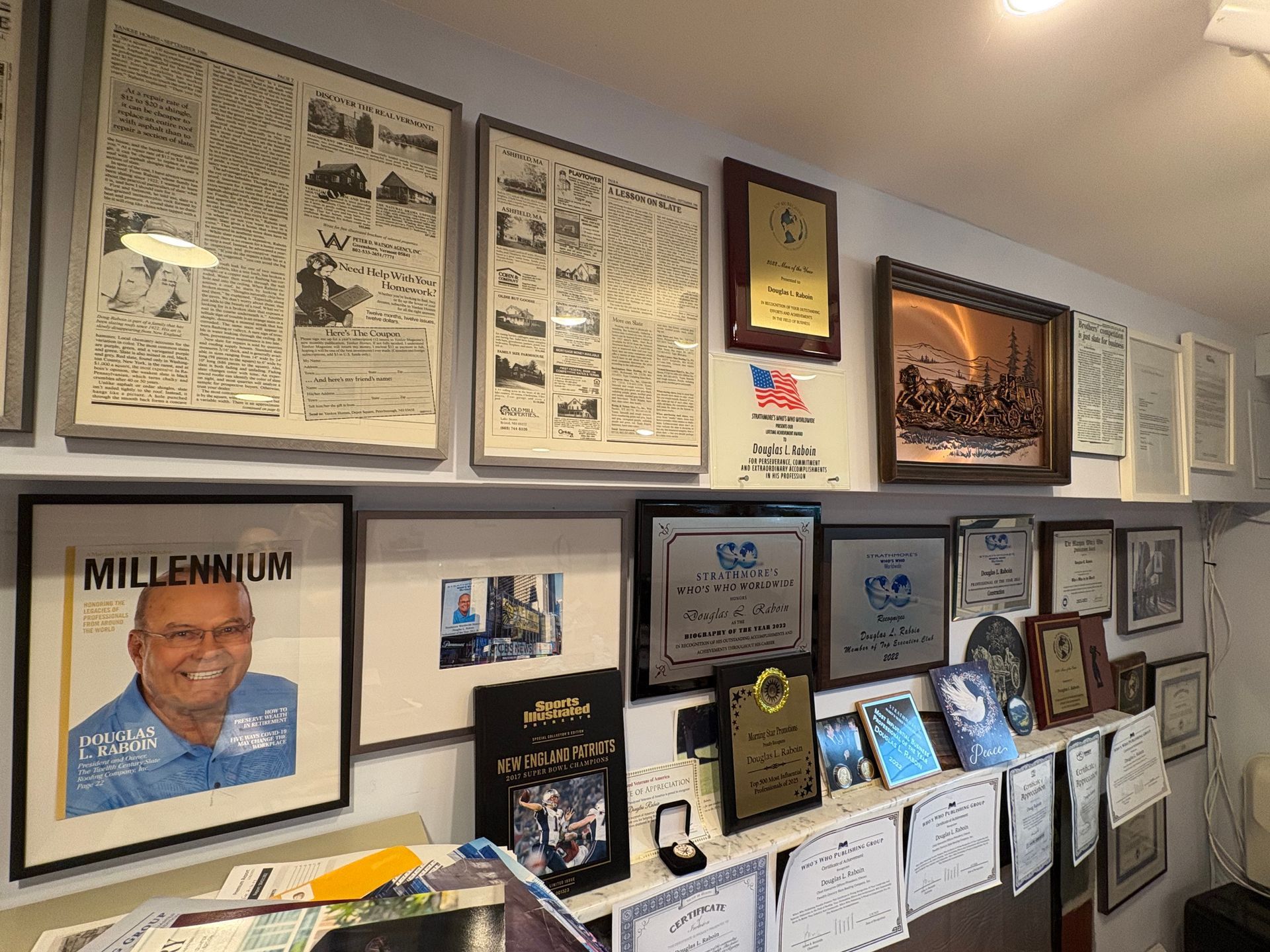 Framed certificates and photos arranged on a wall display, with a large portrait on the left.
