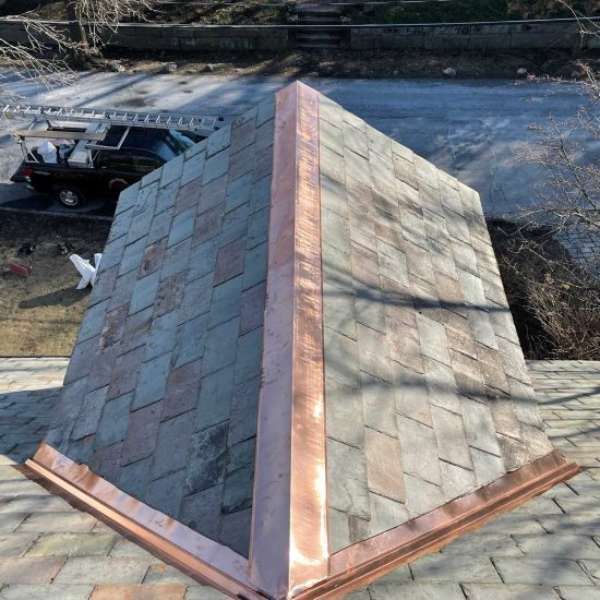 Triangular roof with green shingles and copper flashing, viewed from above outdoors.