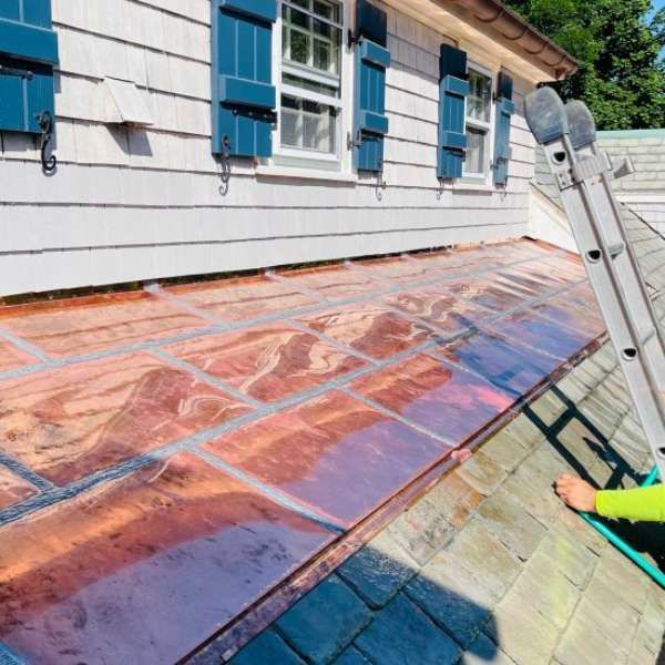 Solar panel installation on a sloped roof beside a white house with blue shutters; worker visible at lower right