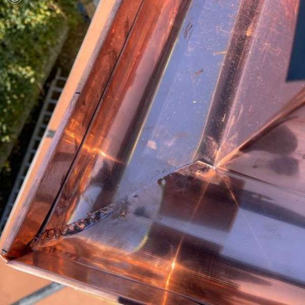 Copper-toned geometric glass skylight with reflective panels and a small water droplet on the surface