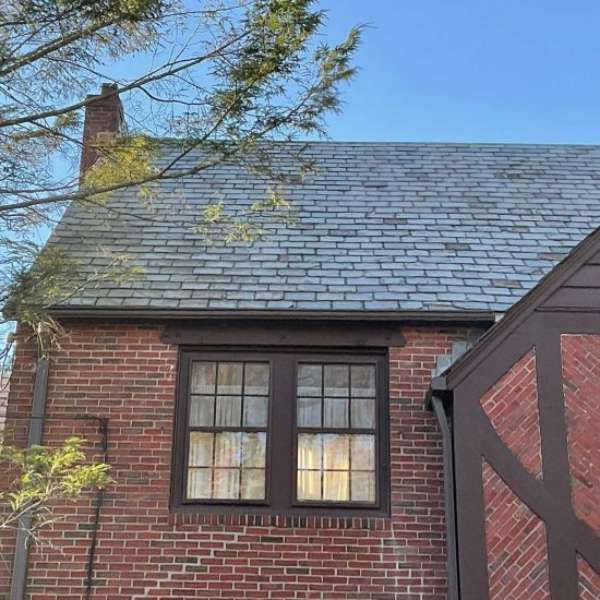 Brick house roofline with two lit windows and a tree branch in front