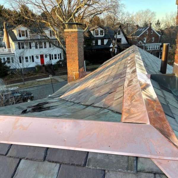 Rooftop copper ridge and brick chimney overlooking suburban houses at dusk