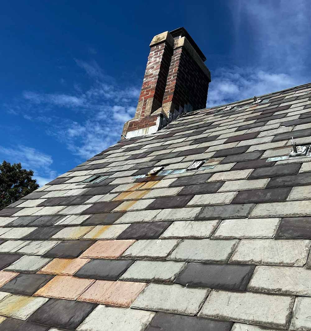 Steep slate roof with a brick chimney against a blue sky
