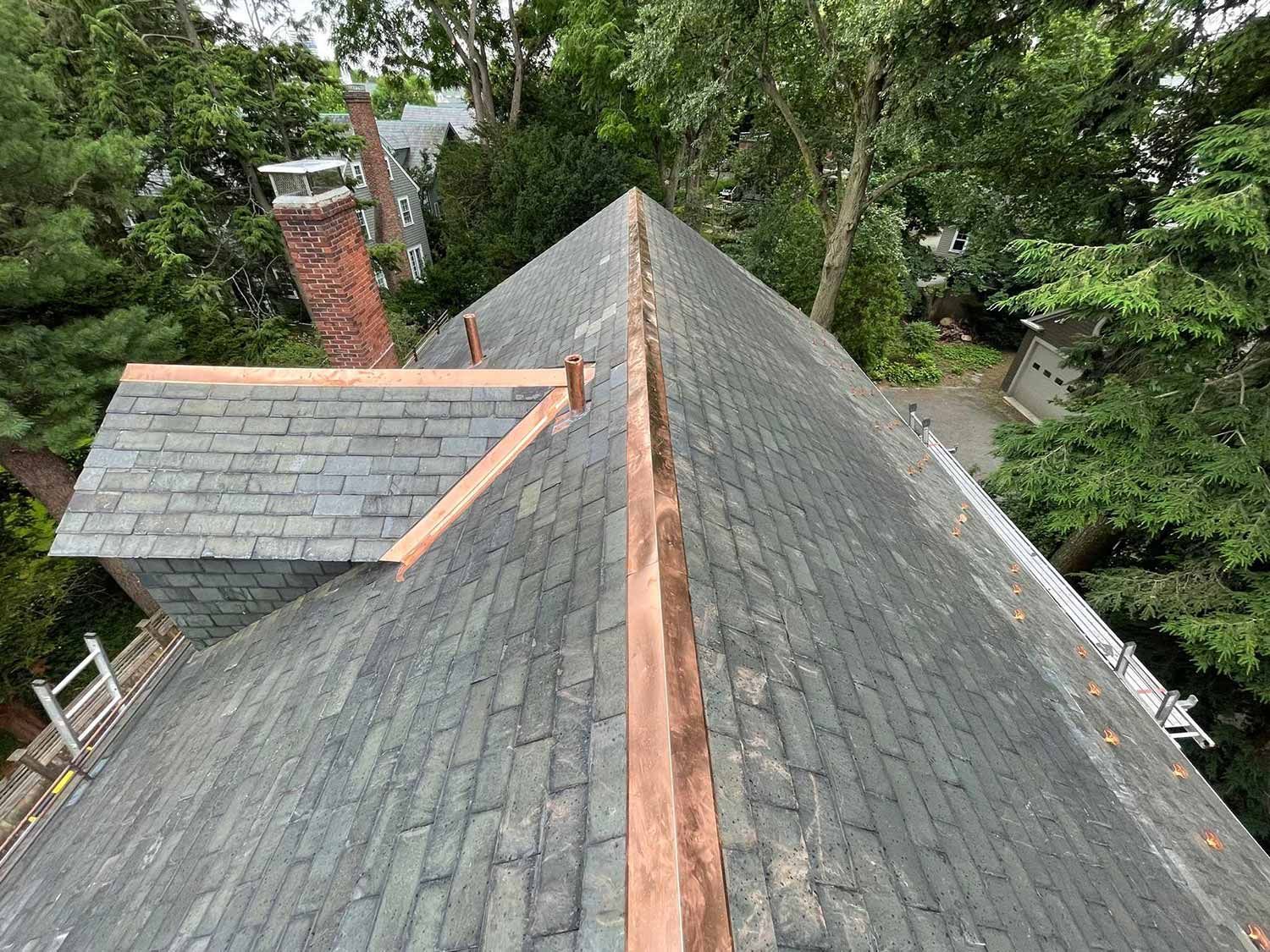 Aerial view of a gray shingled roof with a central ridge, surrounded by trees.