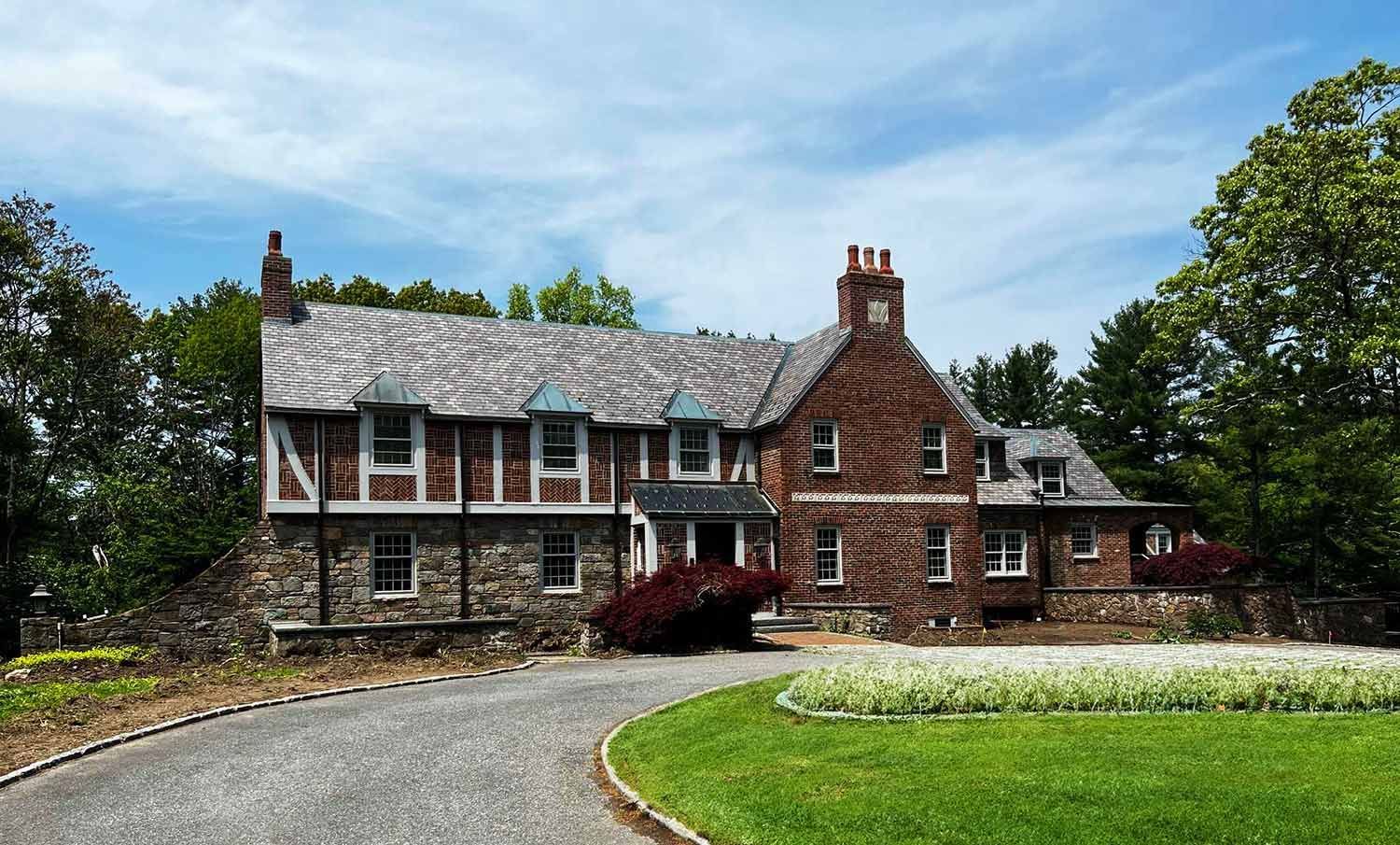 Stone-and-brick farmhouse with a curved driveway, green lawn, and blue sky