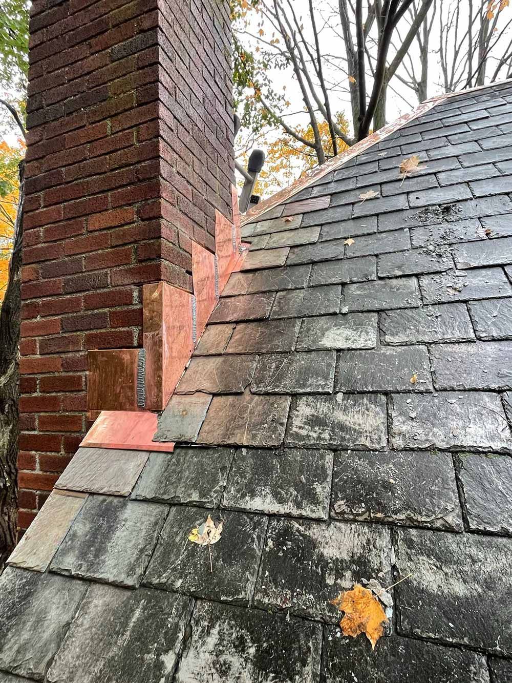 Brick chimney beside a slate roof with autumn leaves scattered on the shingles