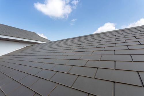 Dark gray shingle roof under a blue sky with clouds