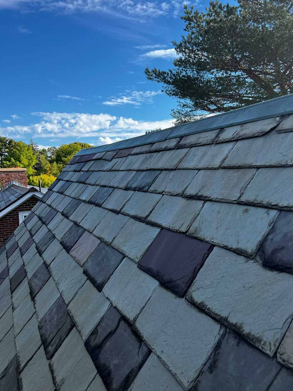 Slate roof under a bright blue sky with clouds and trees in the background