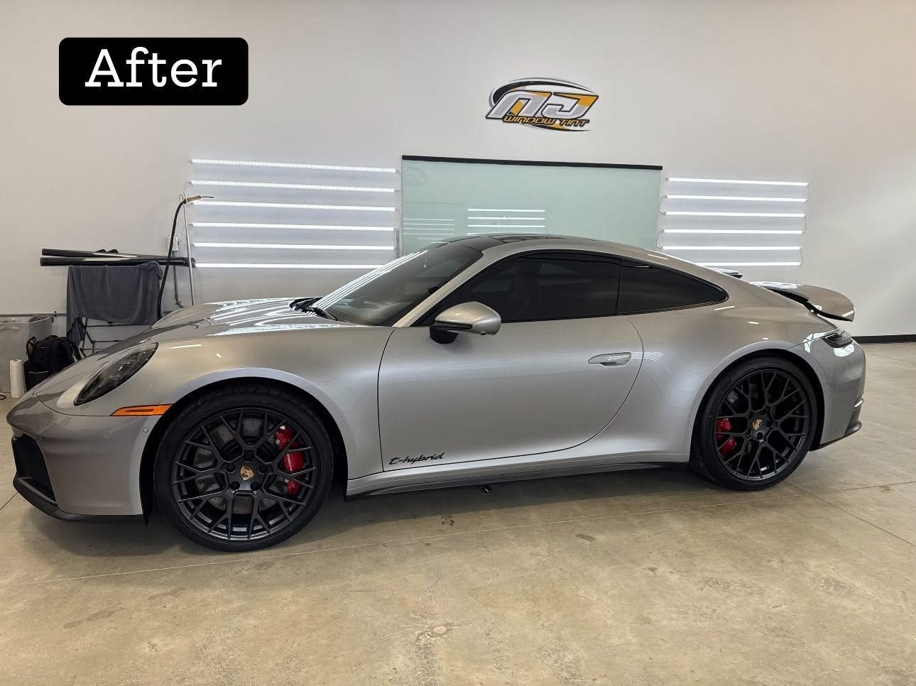 Silver Porsche with tinted windows, black wheels, and red brake calipers in a shop.