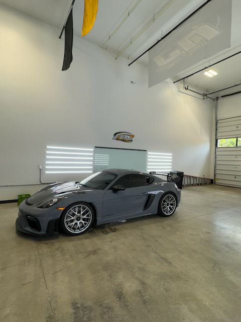 Gray Porsche sports car in a large, white garage, with a ramp and open door visible.