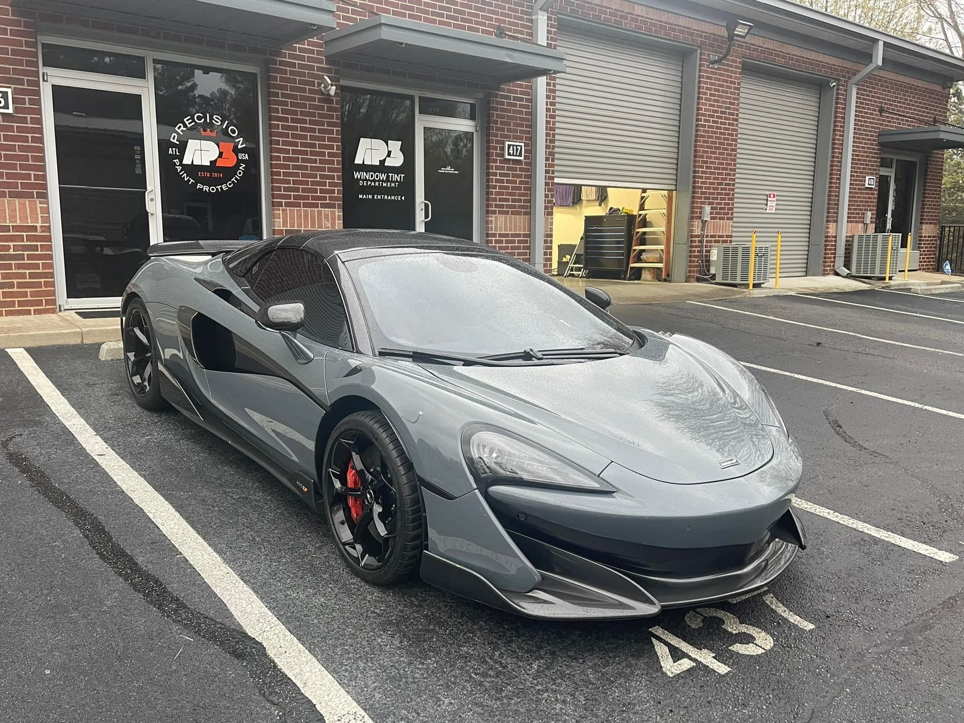 Gray McLaren sports car parked in front of a building with garage doors.