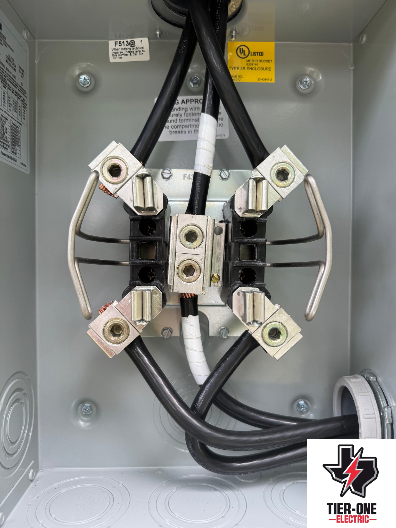 Electrical panel with connected black cables and silver connectors inside a metal box. - after