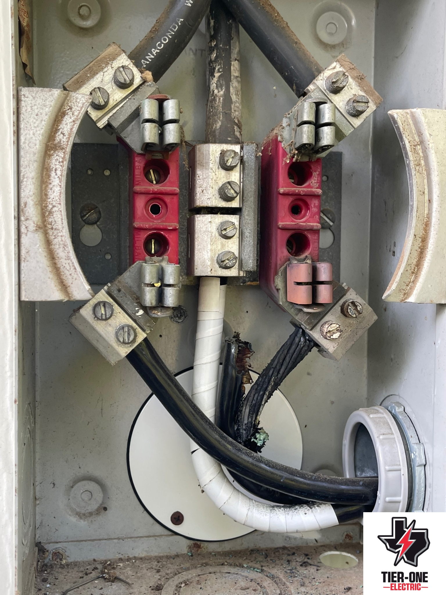 Electrical panel with connected black cables and silver connectors inside a metal box. - before