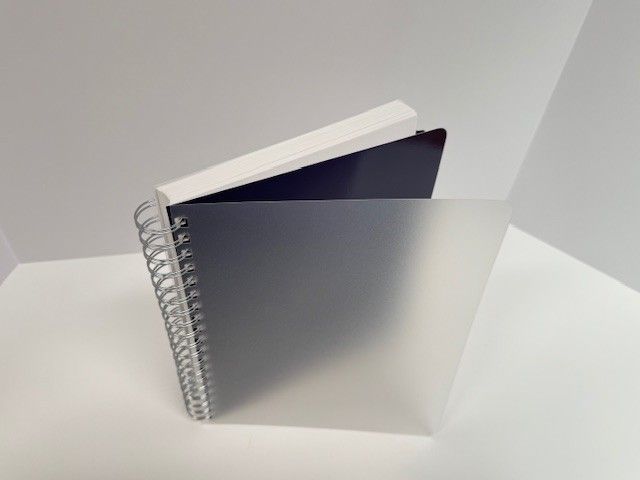 Spiral-bound notebook with white cover, partially visible, inside a frosted gray cover.