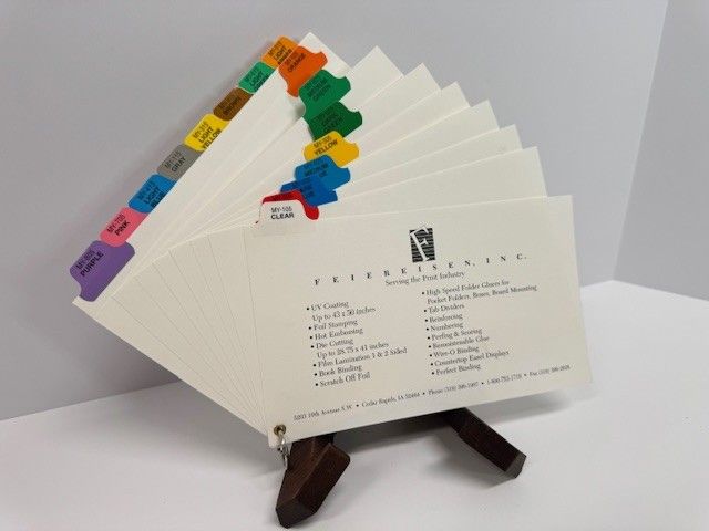 A stack of cream-colored index cards with colored tabs, displayed on a small wooden easel.