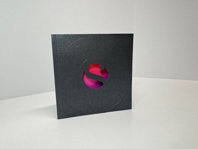 Black box with a circular, magenta and purple logo cut-out in the center.