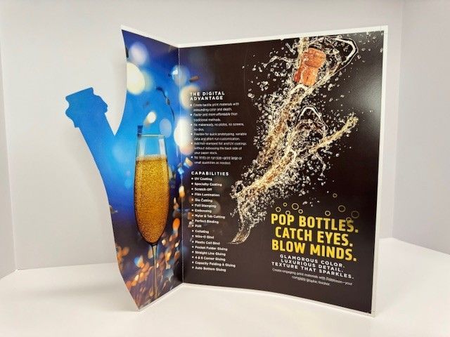 Two-page promotional display with a champagne theme, featuring a glass, popping cork.
