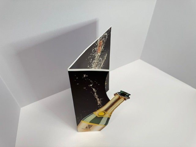 Pop-up card with a champagne bottle and celebratory spray against a dark background, in a white corner.