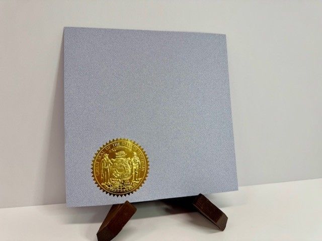 A gray square document with a gold seal, displayed on a wooden easel.