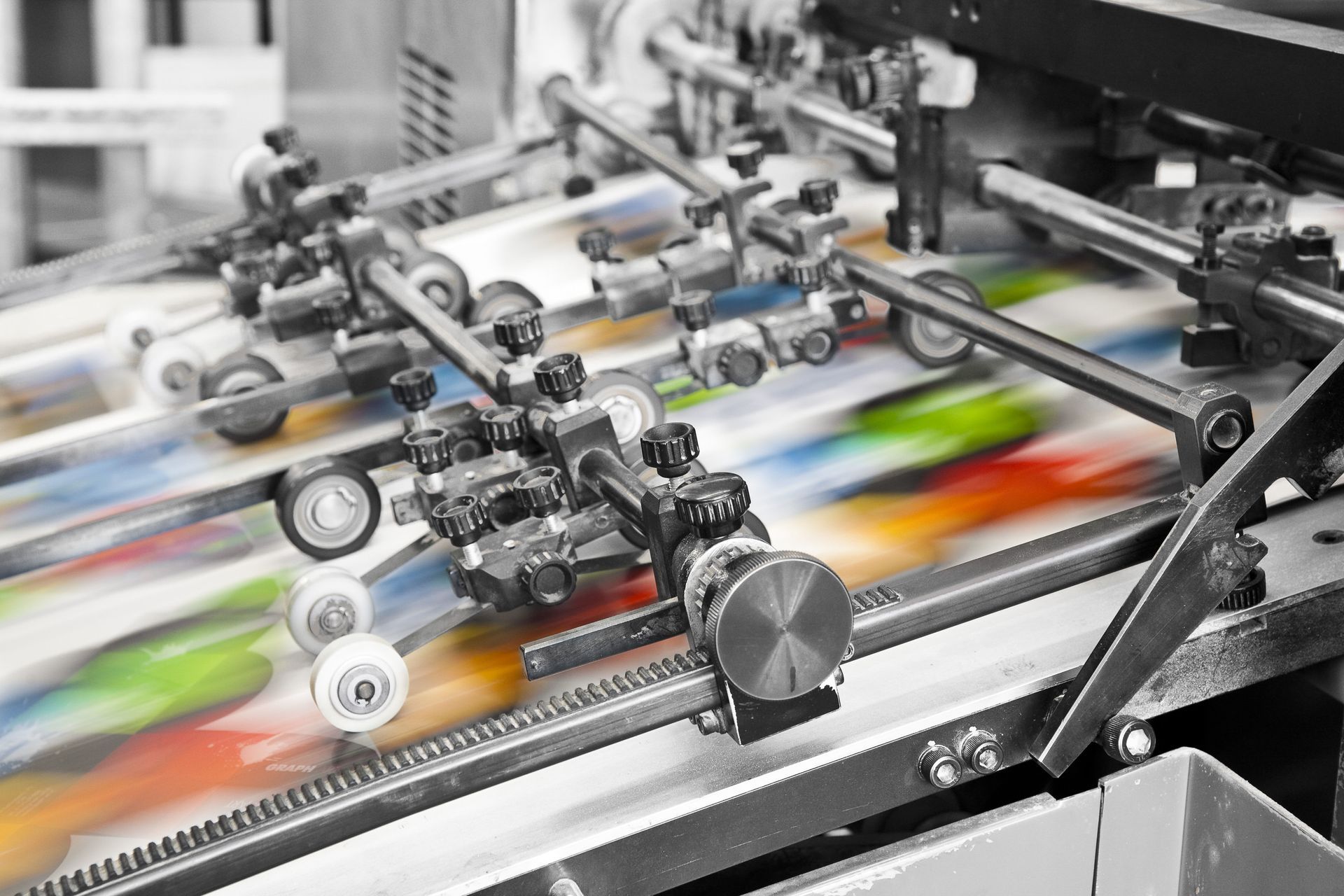 Printing press in operation; colorful paper sheets moving through rollers.