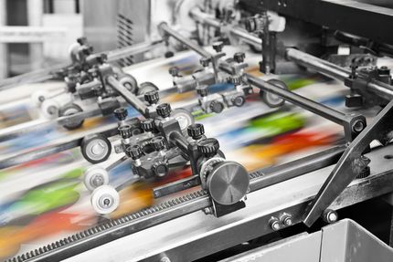 Printing press in operation; colorful paper sheets moving through rollers.