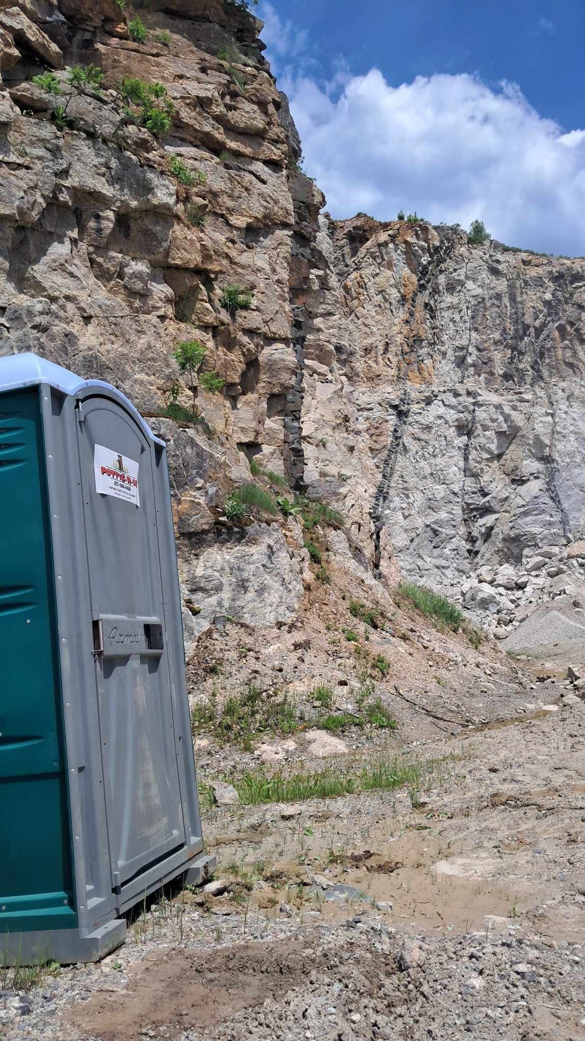A portable toilet is sitting in front of a rocky cliff.