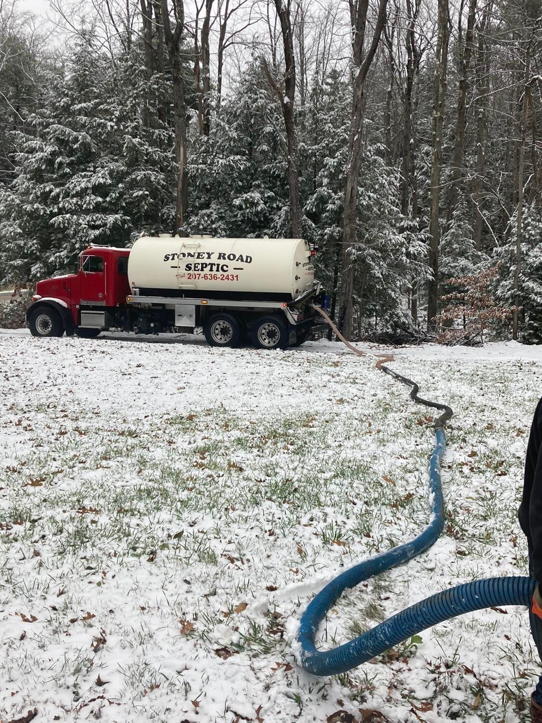 A septic tank truck is parked in the snow with a hose attached to it.