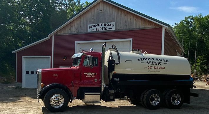 A septic truck is parked in front of a red barn