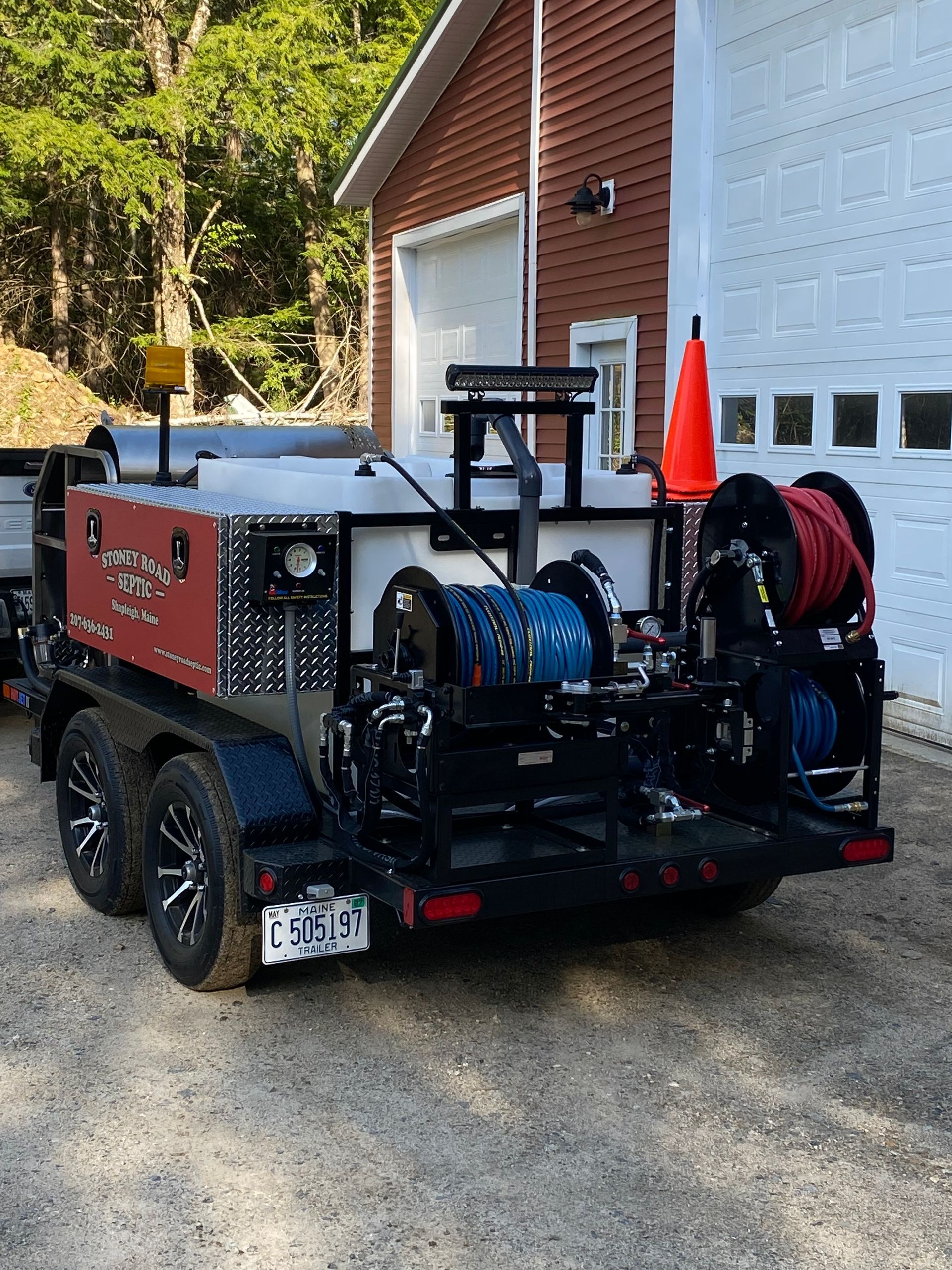 A trailer with a hose attached to it is parked in front of a garage.